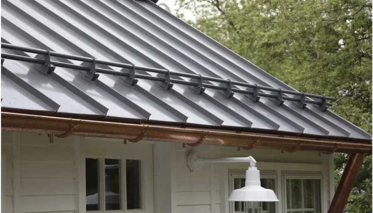 A close-up of a modern metal roof with copper gutters and a white outdoor lamp.